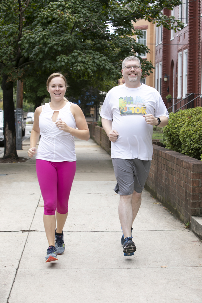 Two runners jog side-by-side down a sidewalk.